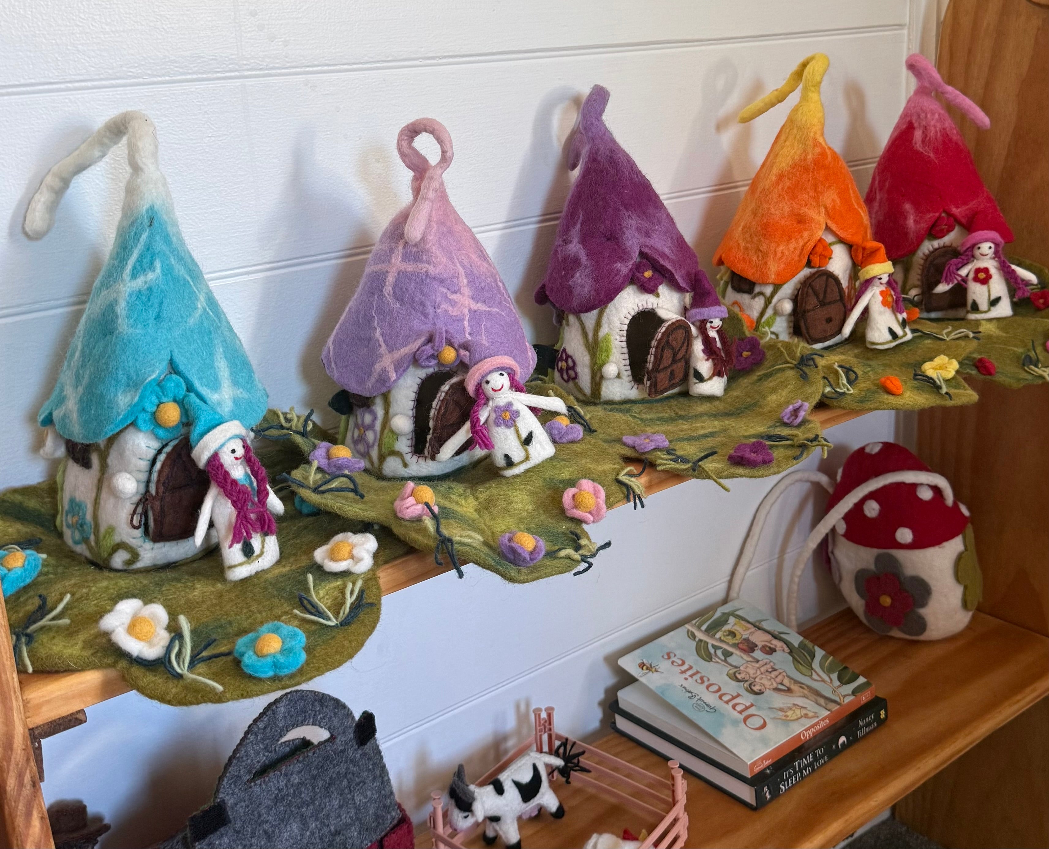 Felted gnome houses with colorful roofs on a shelf with books and toys.