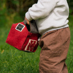 Child holding a red toy barn in a grassy outdoor setting