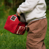 Child holding a red toy barn in a grassy outdoor setting