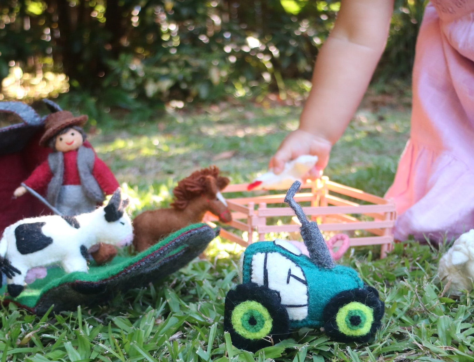Children's toy farm set on grass with a child in pink dress partially visible