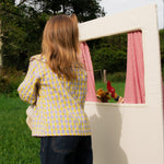 Child playing with a small white playhouse in a grassy area with trees in the background