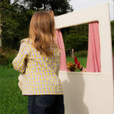 Child playing with a small white playhouse in a grassy area with trees in the background