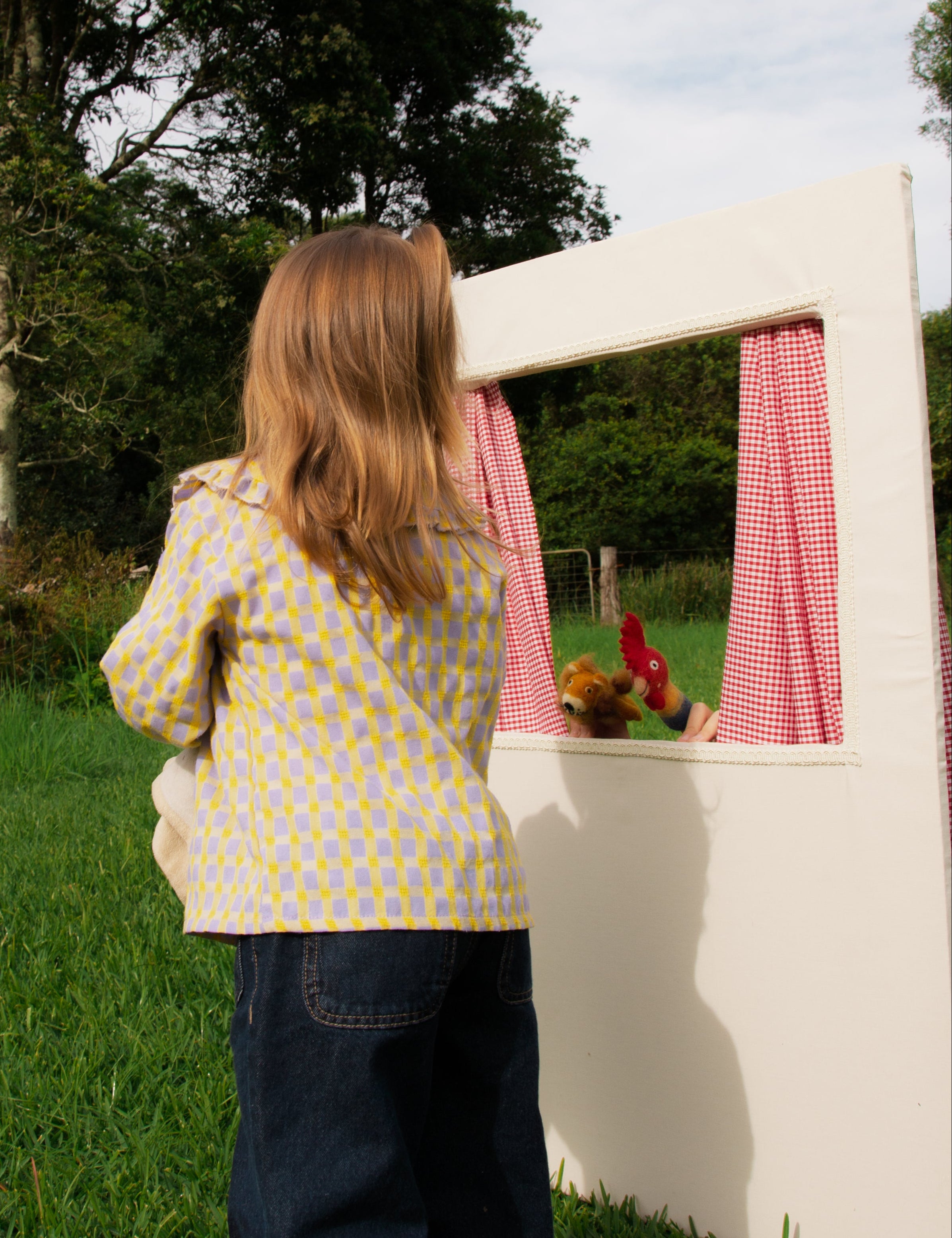 Child playing with a small white playhouse in a grassy area with trees in the background
