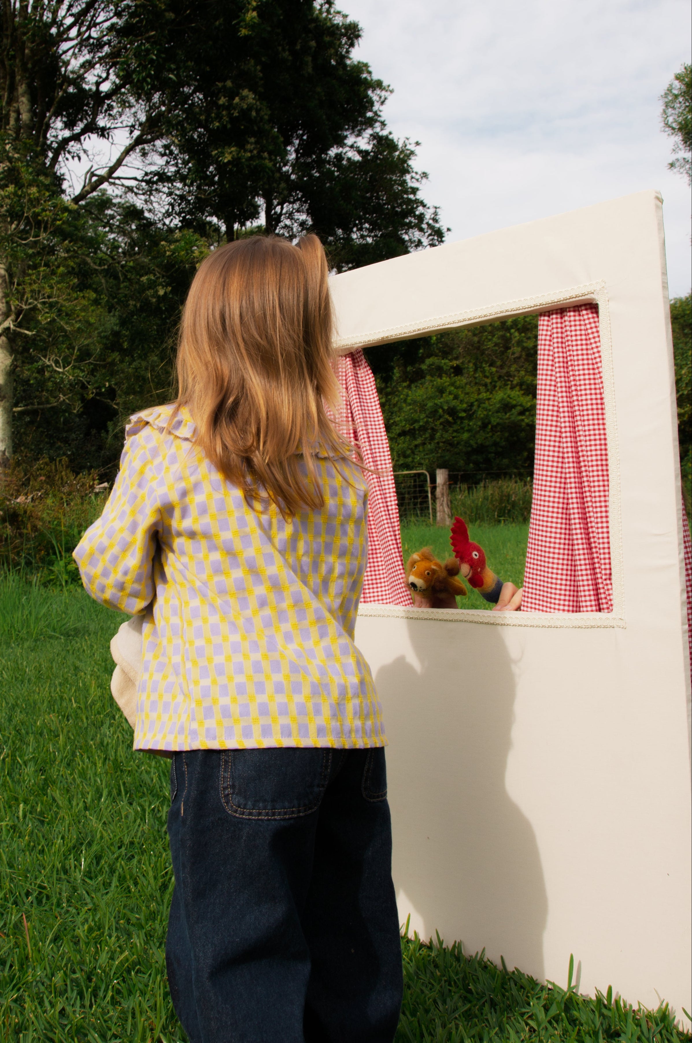 Child playing with a small white playhouse in a grassy area with trees in the background