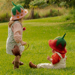 Two children in strawberry hats playing in a grassy field.