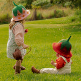 Two children in strawberry hats playing in a grassy field.